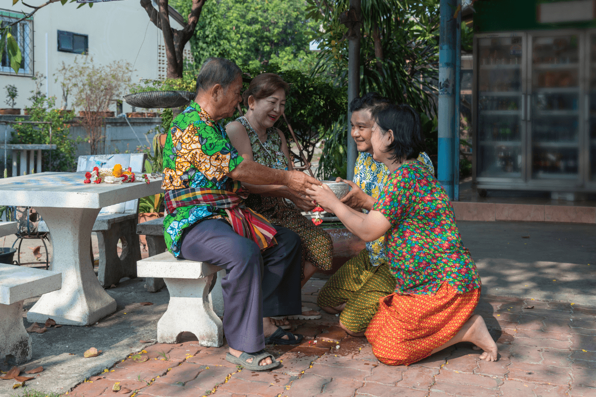 A Thai couple show respect to their elders by kneeling down in front of them and handing them offerings. 